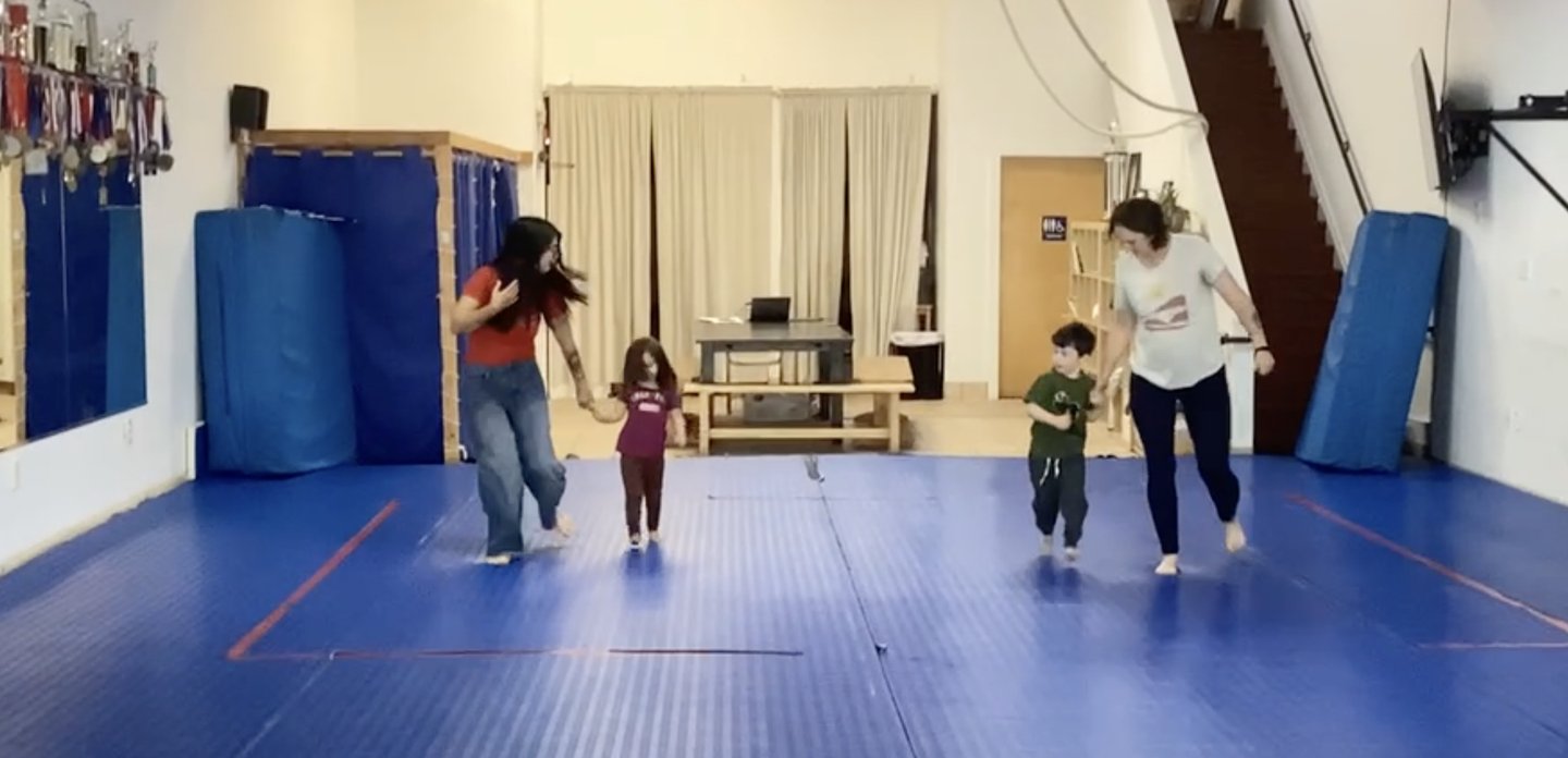 Parents walking hand in hand with their toddlers across the mat during an Oyako class at the Albany dojo