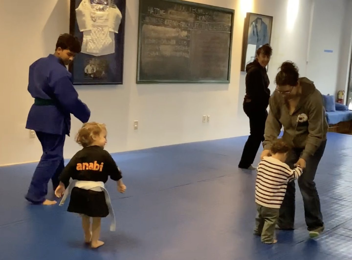 A toddler in a Hanabi Judo gi and white belt on the mat with an instructor during an Oyako parent-and-child class